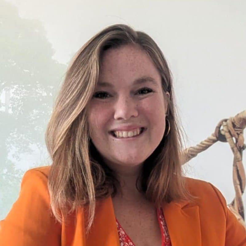 women with shoulder long hair looking into the camera, orange blazer, she smiles