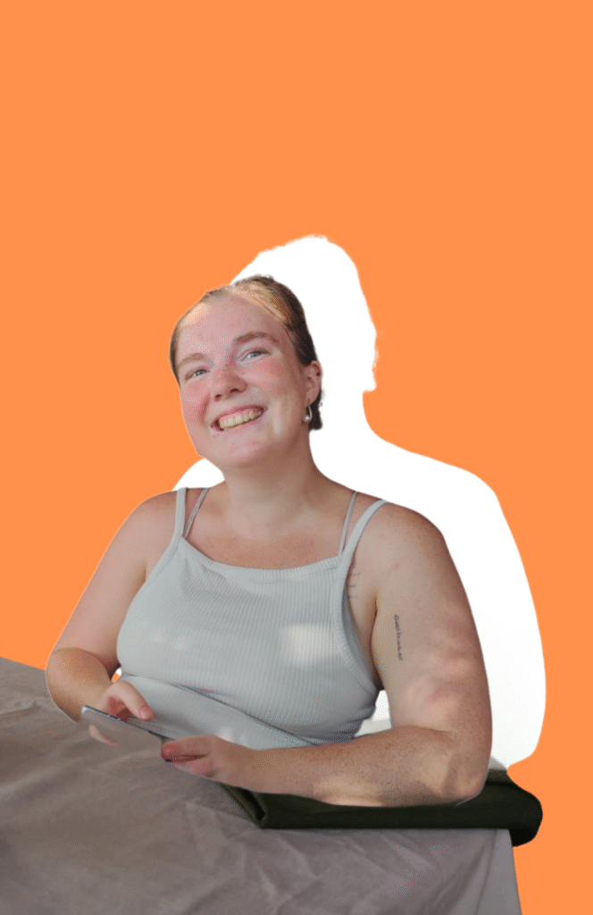 Frau sitzt am Tisch in weißem Top, Hintergrund ist orange